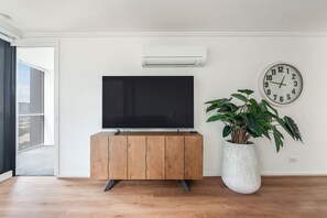 En moderne stue med et fladskærms-tv på et træskab, et hvidt vægur og en potteplante.