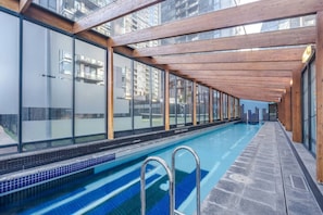 A long indoor swimming pool with glass walls and wooden beams, surrounded by a tiled deck. - Sentinel Vista Urban Stay with Pool and Tennis Court (Southbank)