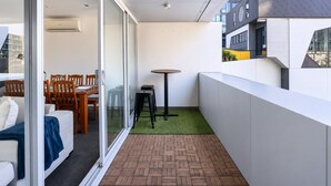 A balcony with a herringbone-patterned floor, a small round table, and a seating area with chairs and a sofa. - Urban Calm Comfortable Base with City Views and Gym (South Yarra)