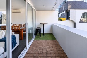 A balcony with a herringbone-patterned floor, a small round table, and a seating area with chairs and a sofa. - Urban Calm Comfortable Base with City Views and Gym (South Yarra)
