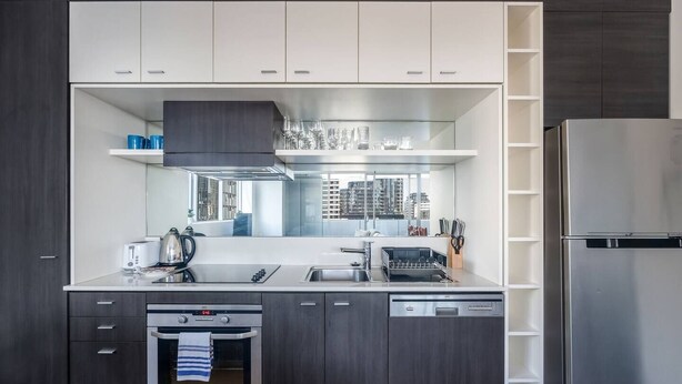 A modern kitchen with built-in appliances, a dishwasher, and a large window providing a view of the city. - Urban Calm Comfortable Base with City Views and Gym (South Yarra)