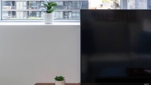 A wooden entertainment center with a flat-screen TV, a small potted plant, and a cabinet with a drawer. - Urban Calm Comfortable Base with City Views and Gym (South Yarra)