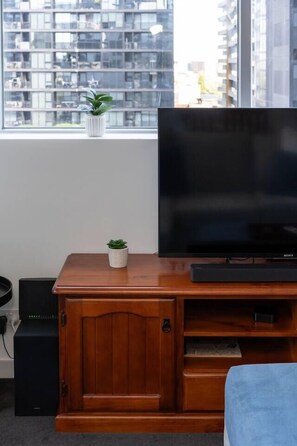 A wooden entertainment center with a flat-screen TV, a small potted plant, and a cabinet with a drawer. - Urban Calm Comfortable Base with City Views and Gym (South Yarra)