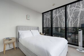 A modern bedroom with a large bed, a nightstand, a wall-mounted TV, and a window with a black mesh screen. - West Edge Urban Outlook near Gardens and Markets (West Melbourne)