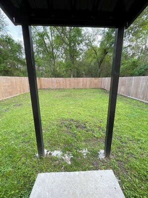 A covered outdoor area with a concrete floor, surrounded by a wooden fence and trees. - Spacious 1,550 Sq Ft Home in Quiet Neighborhood with Private Fenced Backyard (Beaumont)