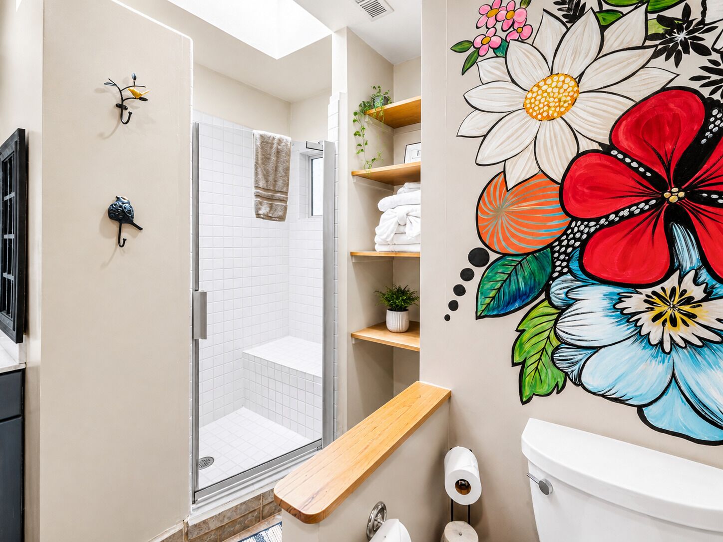 Een badkamer met douche, toilet en een muur met een bloemenmural.