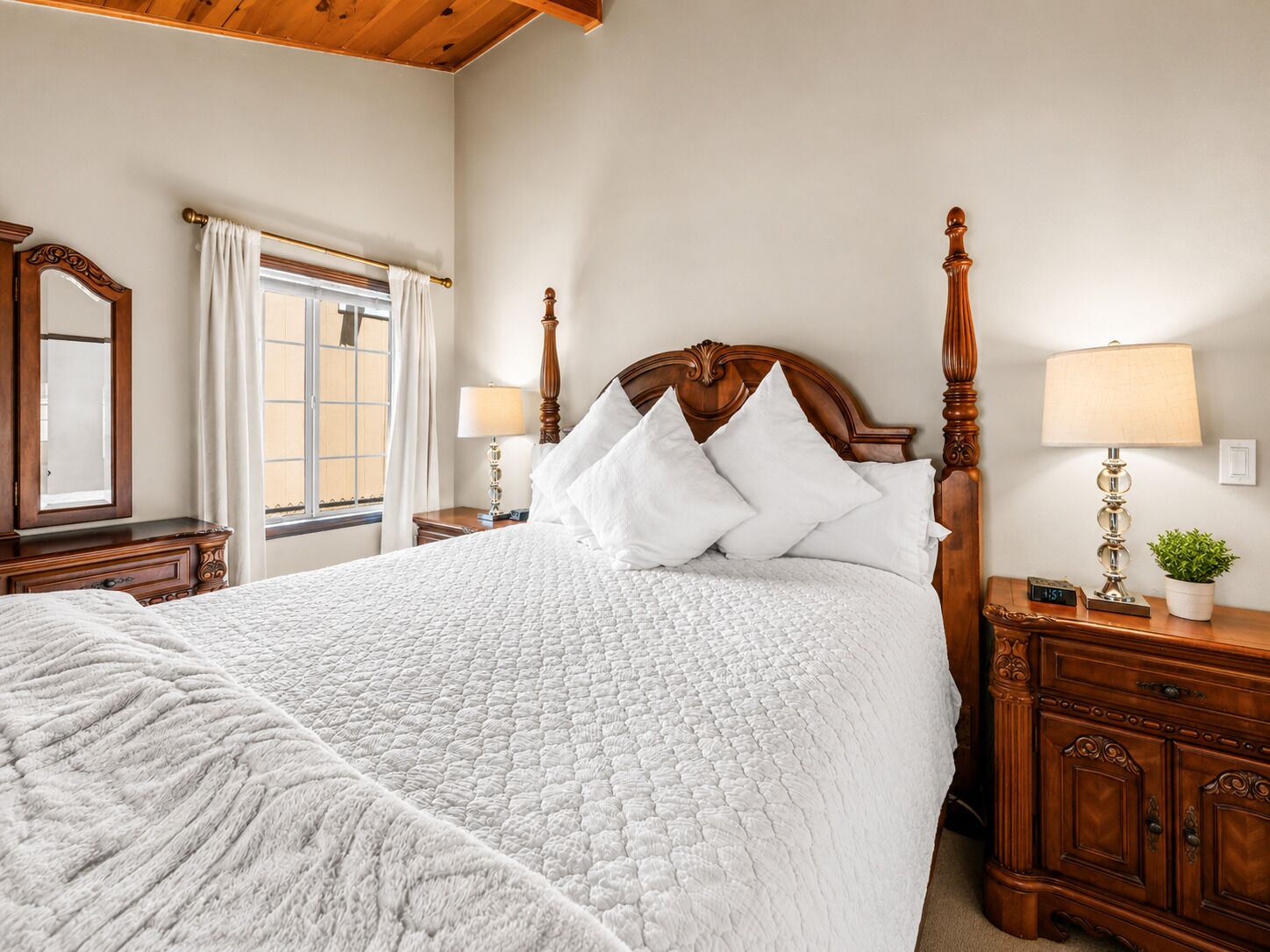 Una cama bien hecha con un edredón blanco acolchado, un cabecero de madera y dos lámparas de noche.
