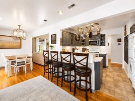 A modern kitchen with a central island, dark wooden chairs, and a dining table with white chairs.