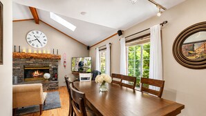 A dining area with a wooden table and chairs, a stone fireplace, and a large window with curtains.