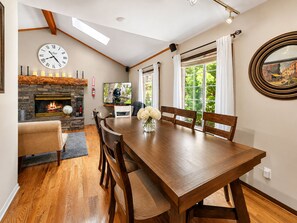 A dining area with a wooden table and chairs, a stone fireplace, and a large window with curtains.