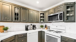 A kitchen with dark green cabinets, a white countertop, a stainless steel microwave, a gas stove, and a dishwasher.