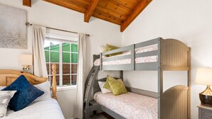 A bedroom with a bunk bed, a single bed, a window with curtains, a lamp, and a painting on the wall.
