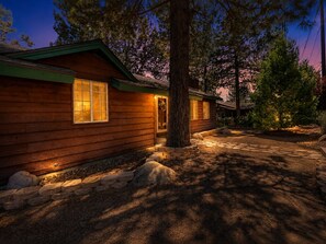 Una cabaña de madera con un camino de piedra que lleva a la entrada, rodeada de árboles.