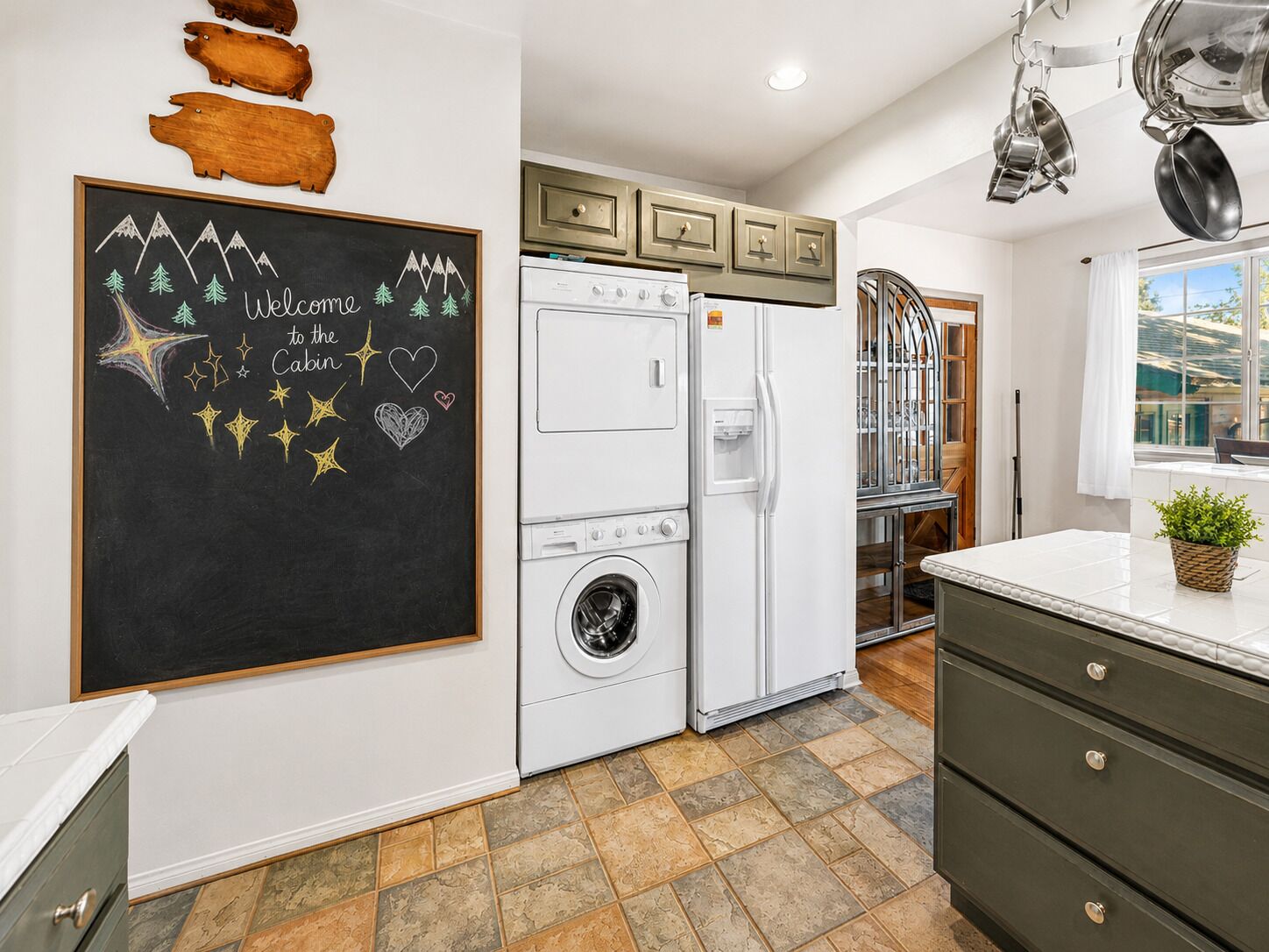 A kitchen with a washing machine, a refrigerator, and a chalkboard with a welcome message.