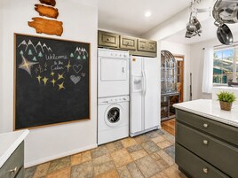 Una cocina con lavadora, refrigerador y una pizarra con un mensaje de bienvenida.