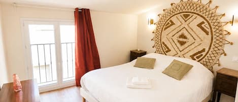 A bedroom with a large bed, a wooden nightstand, a bedside table, a red curtain, and a view through a glass door.