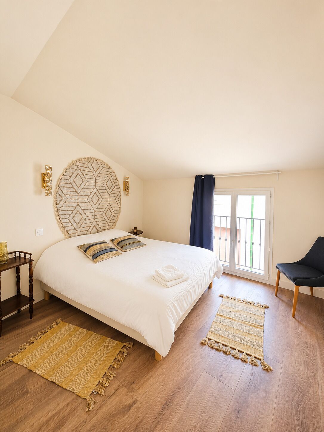 A bedroom with a bed, a nightstand, a chair, and a large window with curtains.
