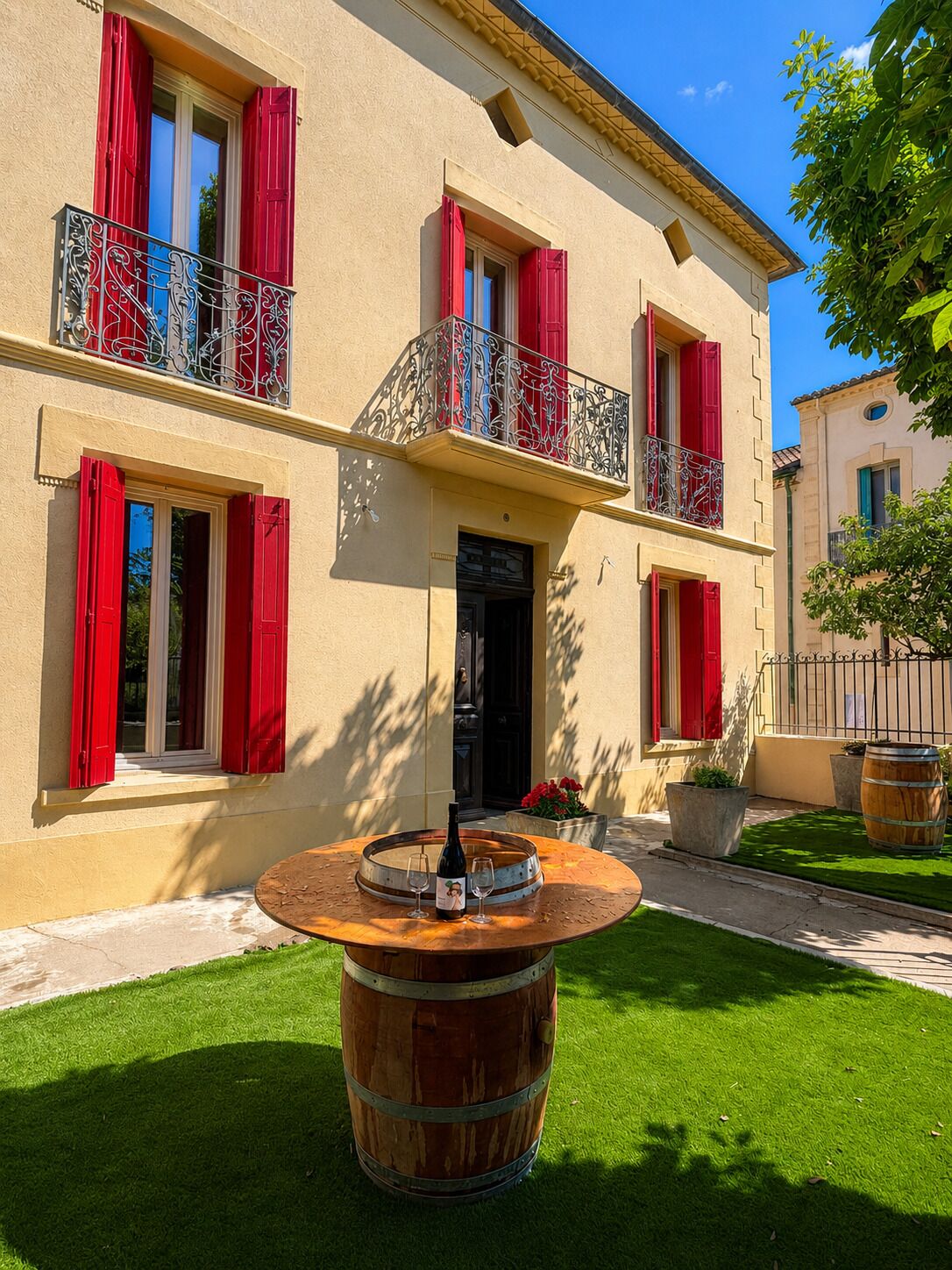 A two-story building with red shutters and a balcony with ornate metal railings.