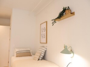 Ein Schlafzimmer mit einem Bett, Kissen, einem an der Wand befestigten Regal mit einer Pflanze, einem gerahmten Bild und einer Wandlampe.