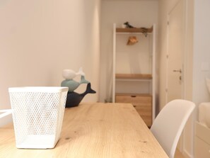 Ein Zimmer mit einem Holztisch, einem weißen Stuhl und einem weißen Korb. Im Hintergrund ist ein Regal mit Dekorationen zu sehen.