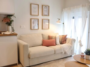 A neutral-colored sofa with decorative pillows, a small round table with a candle, and framed artwork on the wall. - Larrabide Nordic Apartment (Pamplona)