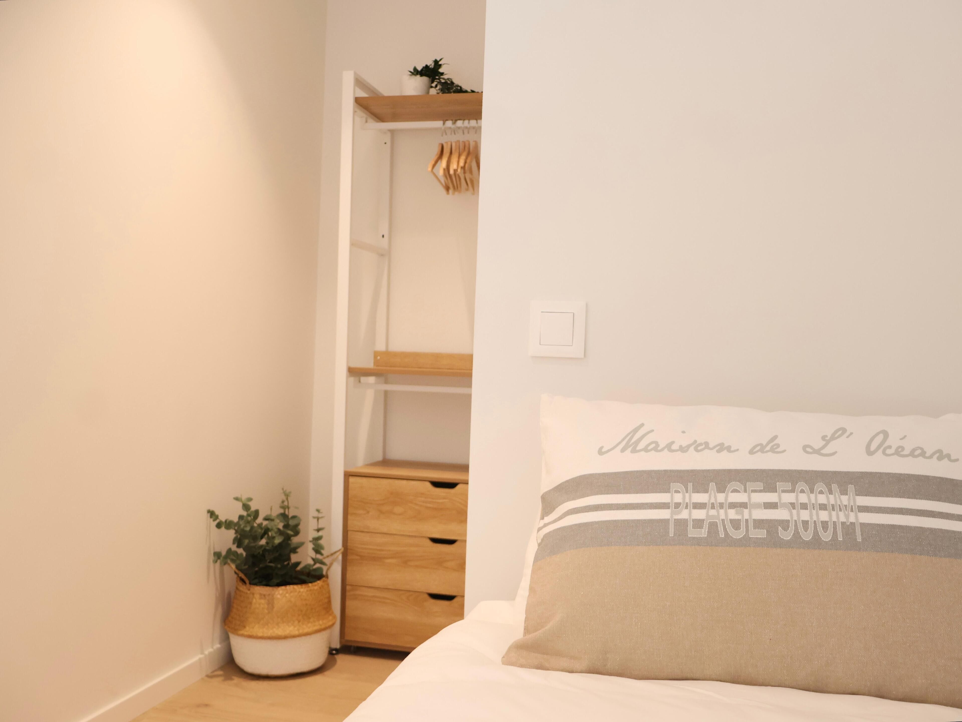 Quarto com cama, mesa de cabeceira, guarda-roupa de madeira e planta em vaso.