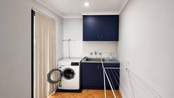 A compact laundry room with a washing machine, a drying rack, and a sink.