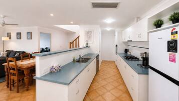 A modern kitchen with white cabinets, a blue countertop, and a gas stove. There is a dining area with a wooden table and chairs.