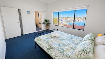 A bedroom with a bed, a window with a marina view, a door, and a small bathroom.