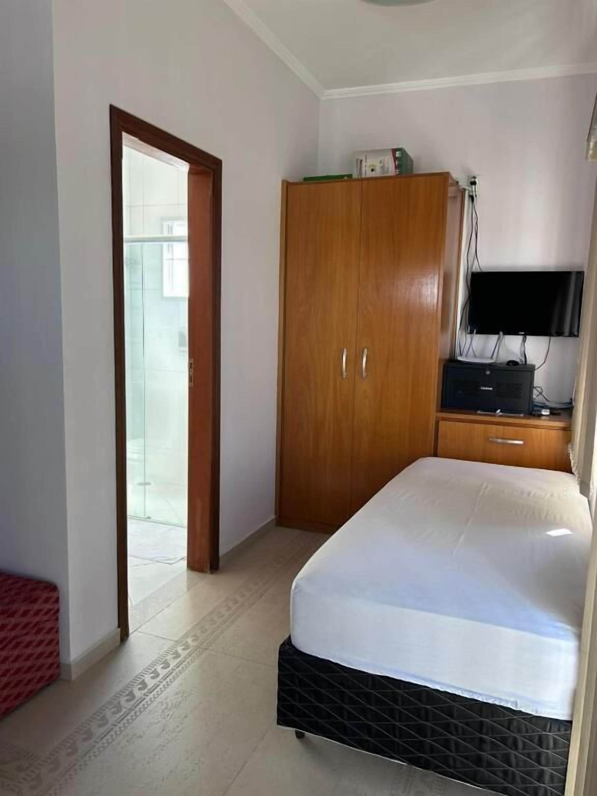 Un dormitorio con cama, armario, televisor y puerta que da a un balcón.
