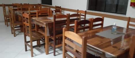 A dining area with wooden tables and chairs, a fire extinguisher on the wall, and a window with blinds.