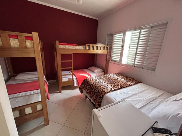 A dormitory room with bunk beds, a window with blinds, and a desk with a keyboard.