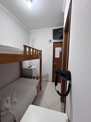 Una habitación pequeña y funcional con una litera, un escritorio con silla, secador de pelo y televisor montado en la pared.