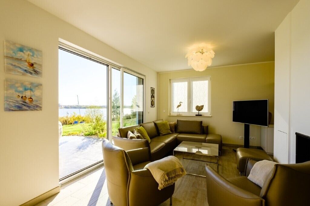 Een moderne woonkamer met een zithoek, een flatscreen televisie en een groot raam met uitzicht op de omgeving.