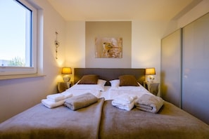 A double bed with two pillows and a blanket, a bedside lamp, a wall-mounted artwork, and a window.