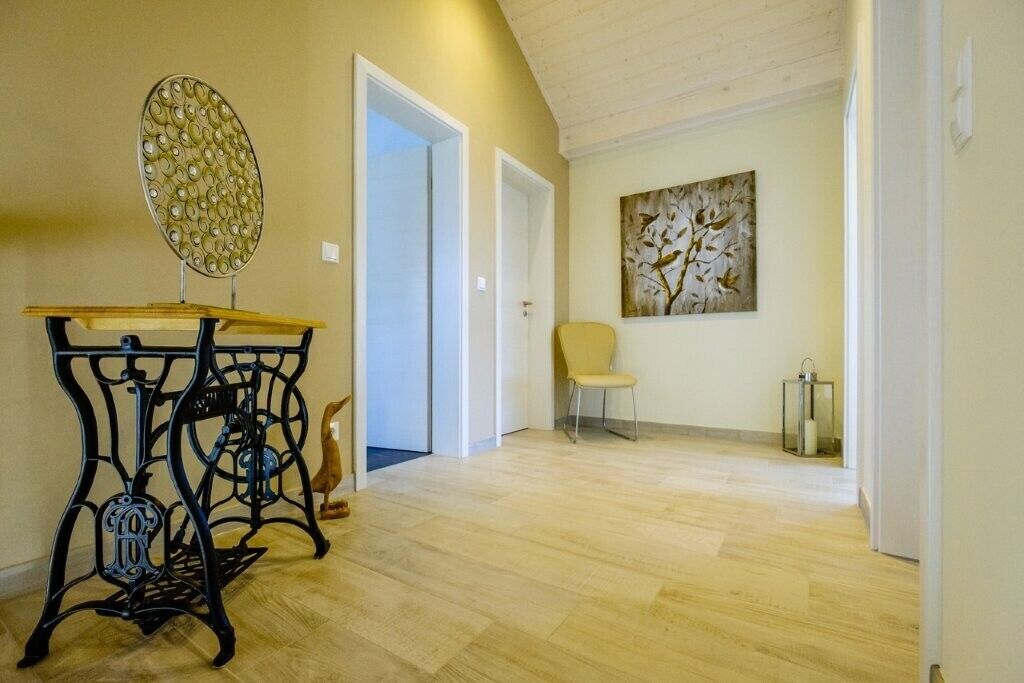 Un pasillo con piso de madera, una silla, una mesa con cubierta decorativa y una obra de arte en la pared.