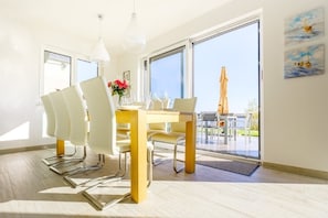 A dining area with a table and chairs, a vase with flowers, and a view through a glass door to an outdoor patio.