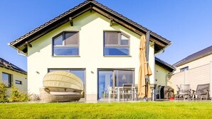 Una casa de dos pisos con techo plano, ventanas amplias y un espacio de estar al aire libre cubierto.