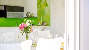 Un área de comedor con una mesa preparada para dos, un florero con flores y una pared verde de fondo.