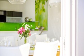 A dining area with a table set for two, a vase with flowers, and a green wall in the background.