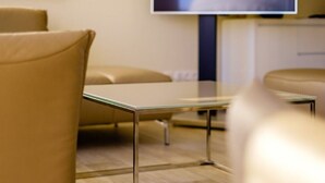 Habitación de hotel moderna con una mesa de vidrio, sillas de cuero y un televisor en la pared.