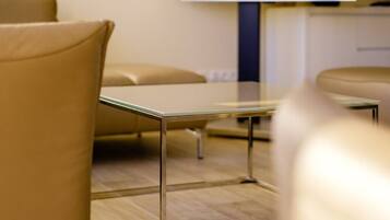 Een moderne hotelkamer met een glazen tafel, lederen fauteuils en een televisie aan de muur.