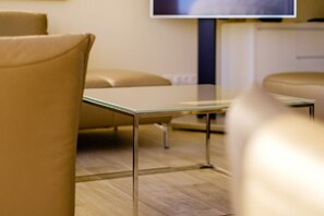 A modern hotel room with a glass table, leather chairs, and a television on the wall.
