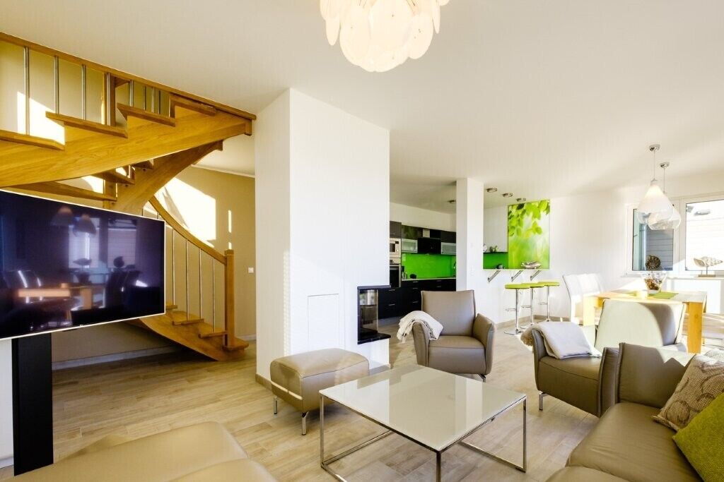 Ein modernes Wohnzimmer mit Flachbildfernseher, Glastisch und einer Treppe, die in eine obere Ebene führt.
