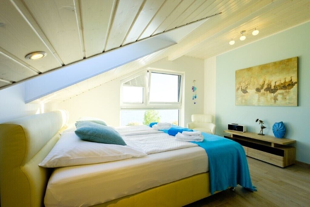 Un dormitorio con cama, ventana, un cuadro y una mesita de noche.