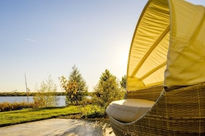 A wicker chair with a cushion, positioned on a patio with a view of a lake and trees.