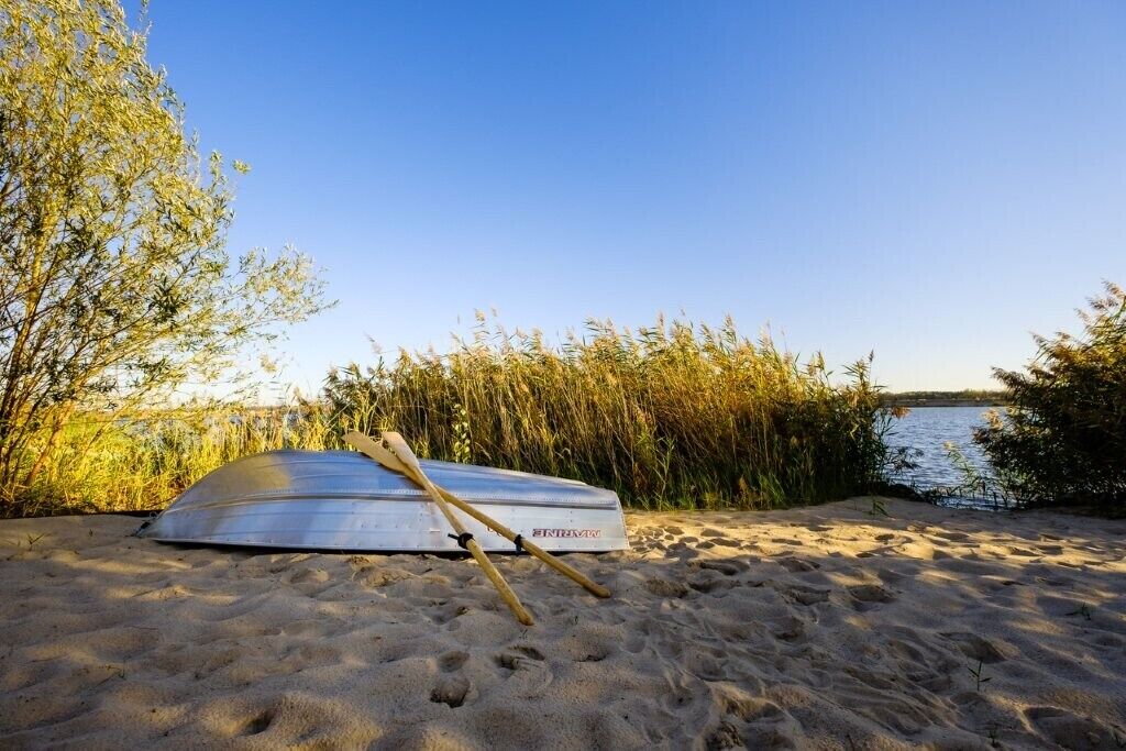 Een kajak op een zandstrand, met water en begroeiing op de achtergrond.