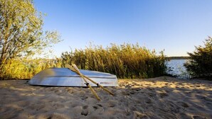 Un kayak sobre una playa arenosa, con agua y vegetación al fondo.