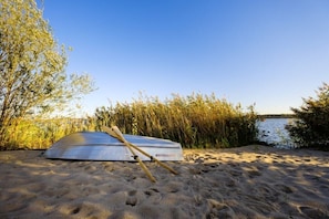 A kayak on a sandy beach with water and vegetation in the background.