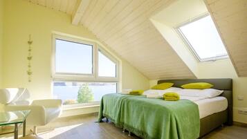 Een slaapkamer met schuine wand, een bed met groen en wit beddengoed, een raam en uitzicht op de omgeving.
